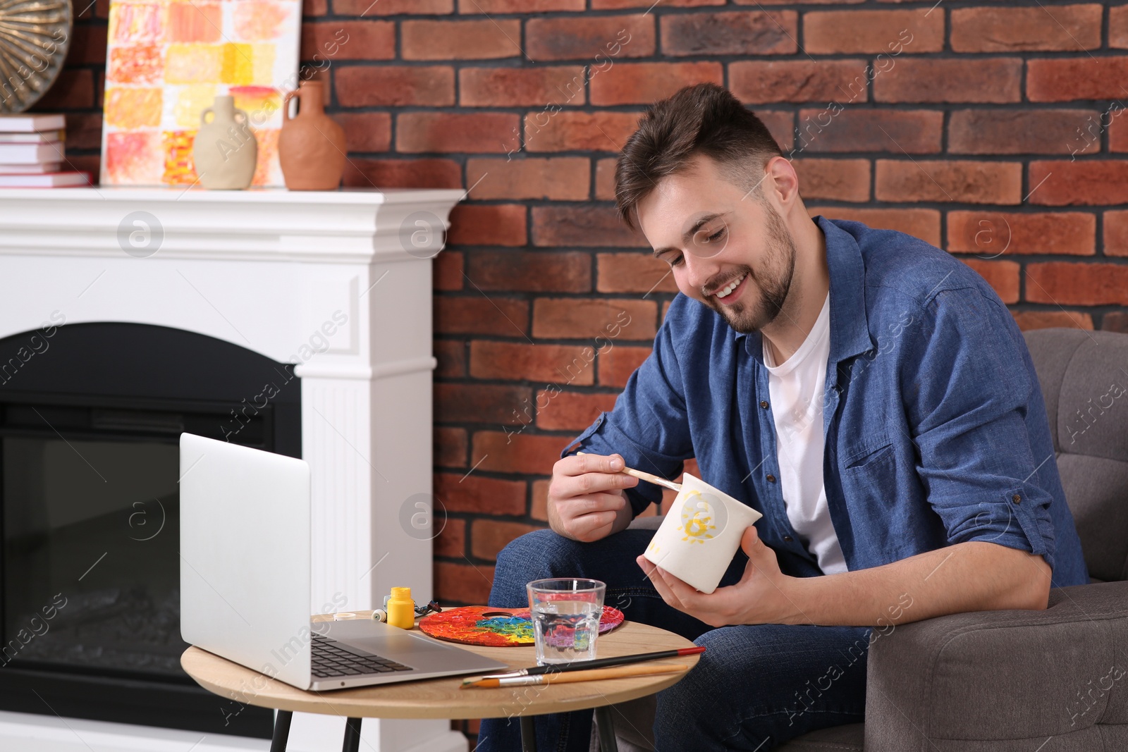 Photo of Happy man learning to decorate cup while watching online course at home. Time for hobby