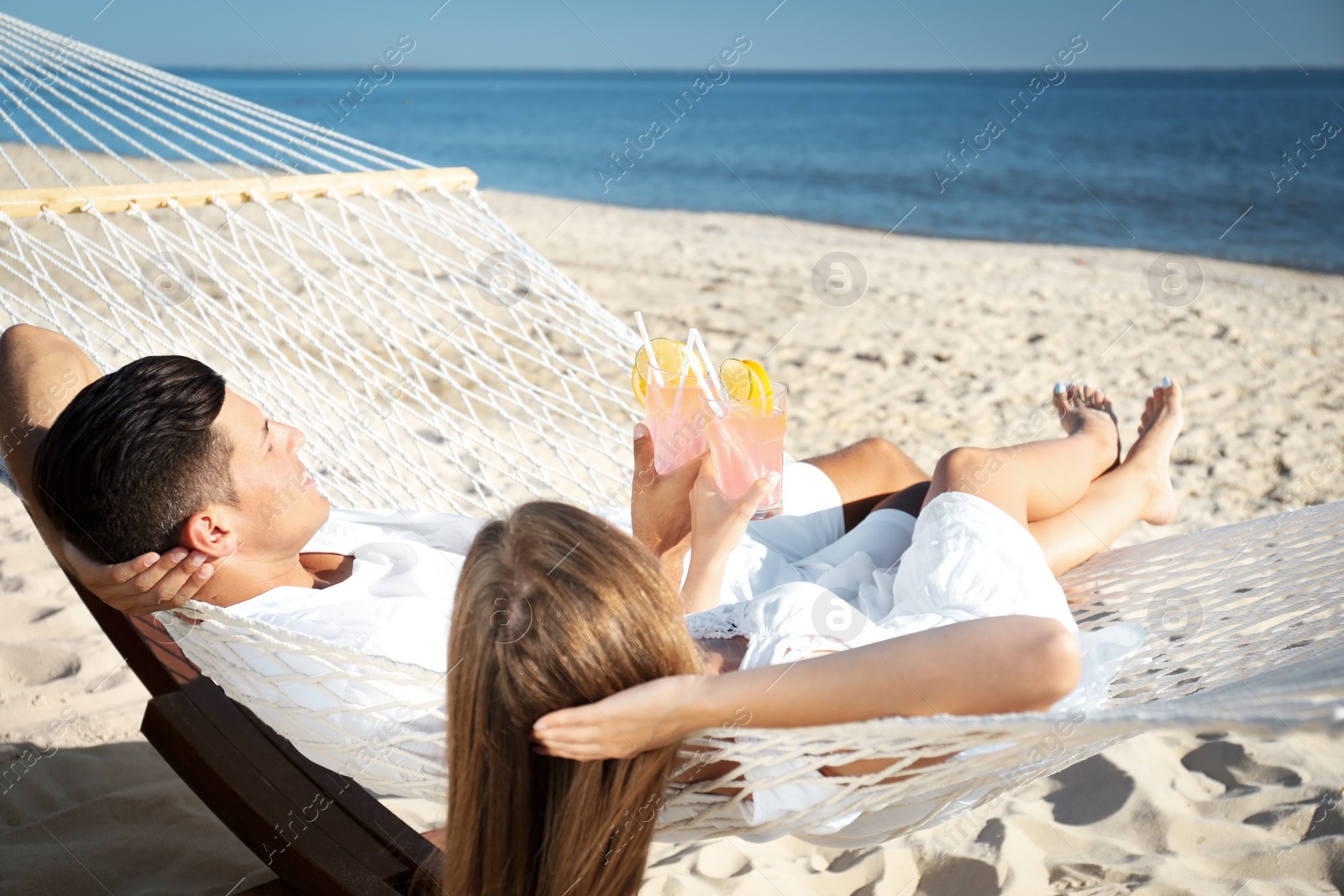 Photo of Couple with refreshing cocktails relaxing in hammock on beach