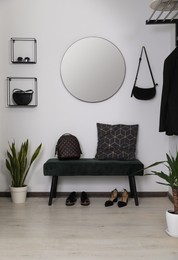 Hallway interior with black bench, shoes and round mirror on light wall