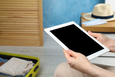 Photo of Woman using modern tablet while packing suitcase for summer vacation at home, closeup