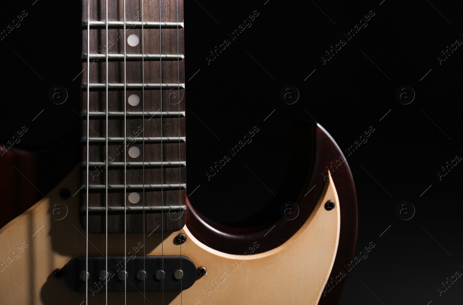 Photo of Modern electric guitar in darkness, closeup view