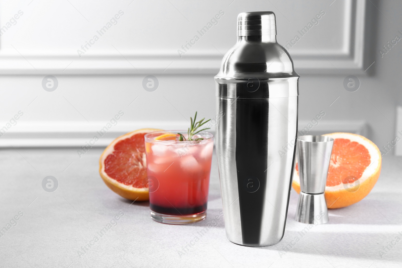 Photo of Metal shaker, delicious cocktail, jigger and grapefruit on light grey table