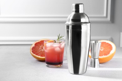 Photo of Metal shaker, delicious cocktail, jigger and grapefruit on light grey table