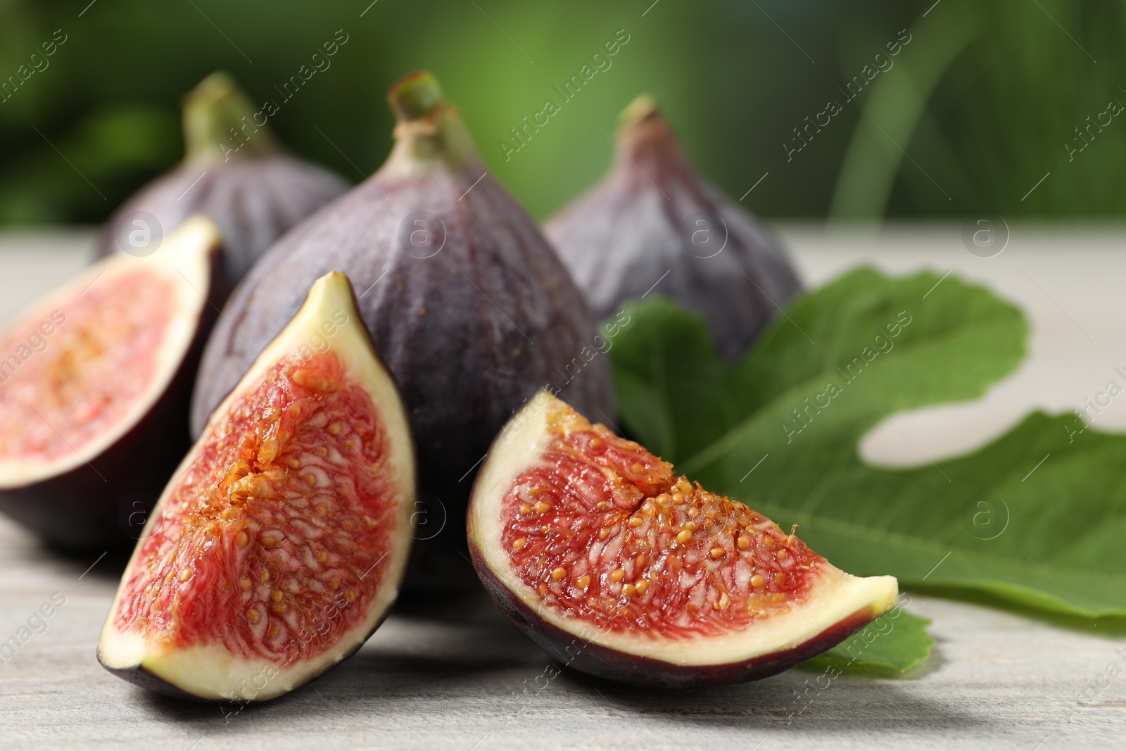 Photo of Whole and cut ripe figs on light wooden table against blurred green background, closeup