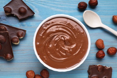 Bowl with tasty paste, chocolate pieces and nuts on light blue wooden table, flat lay