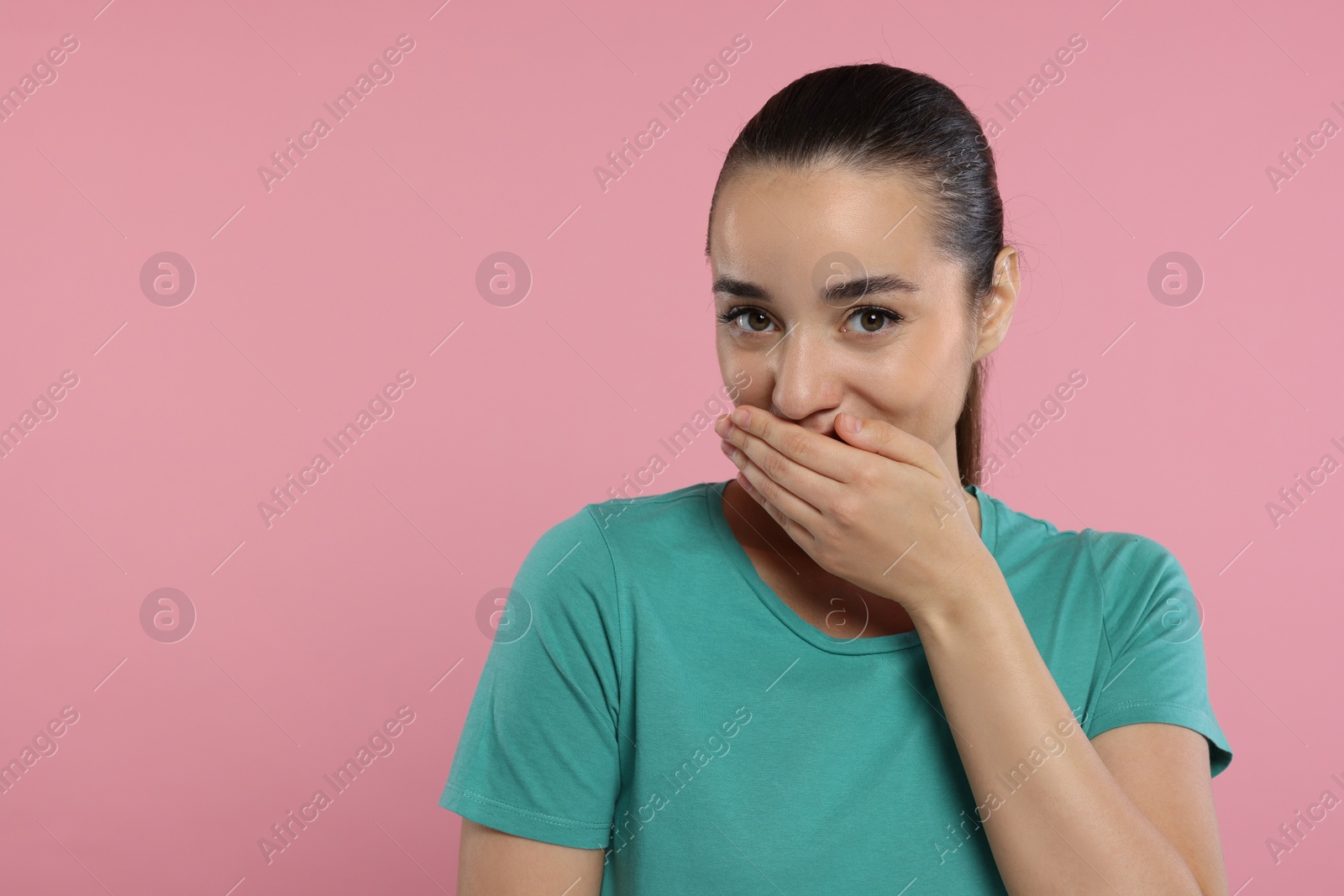 Photo of Embarrassed woman covering mouth on pink background. Space for text