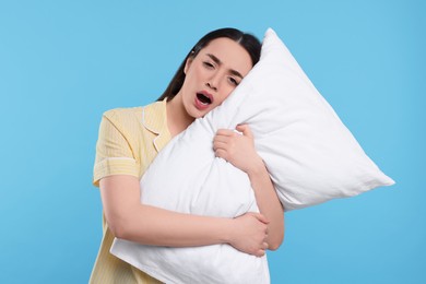 Photo of Tired young woman with pillow yawning on light blue background. Insomnia problem