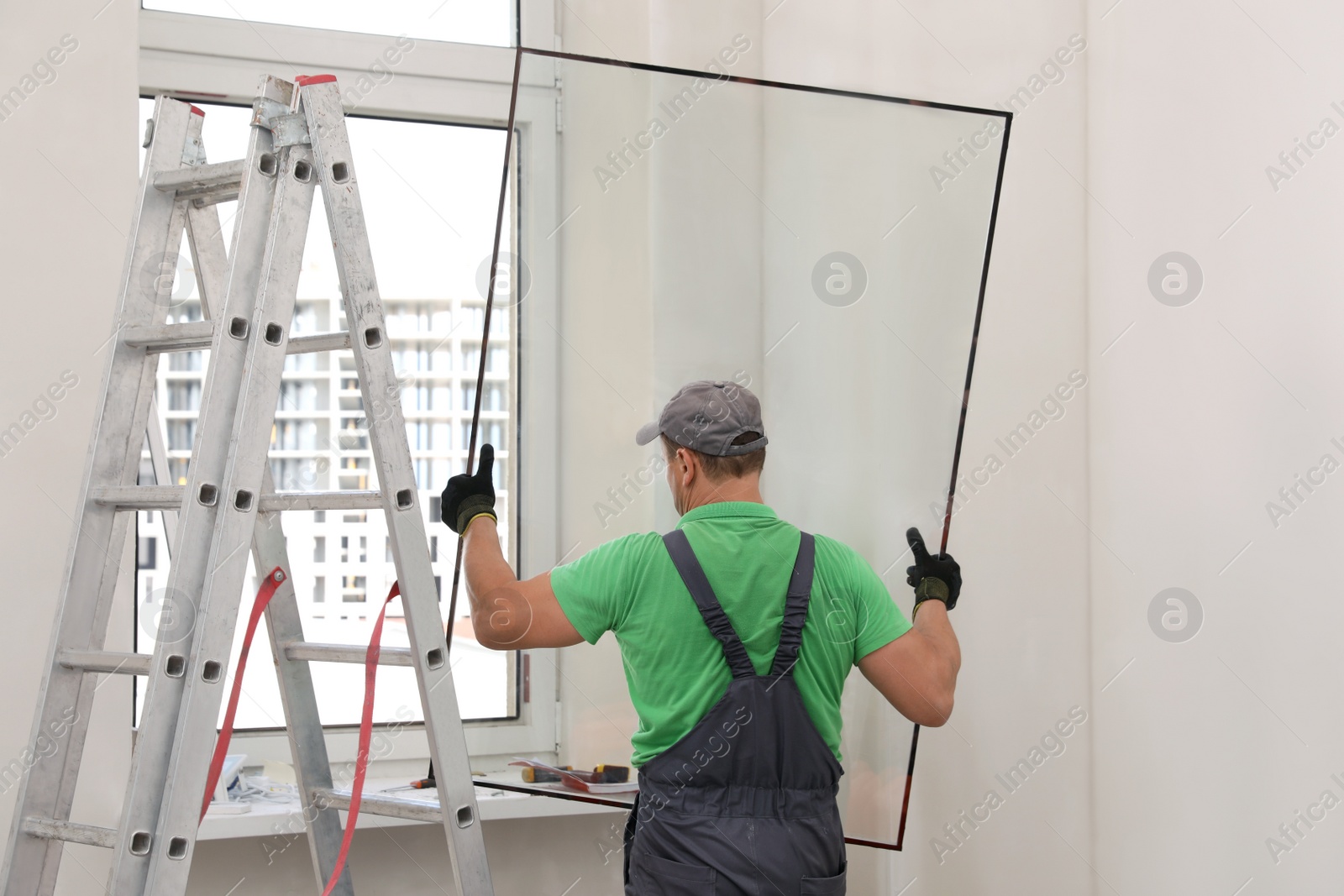 Photo of Worker in uniform holding double glazing window indoors, back view