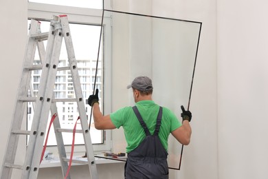 Worker in uniform holding double glazing window indoors, back view