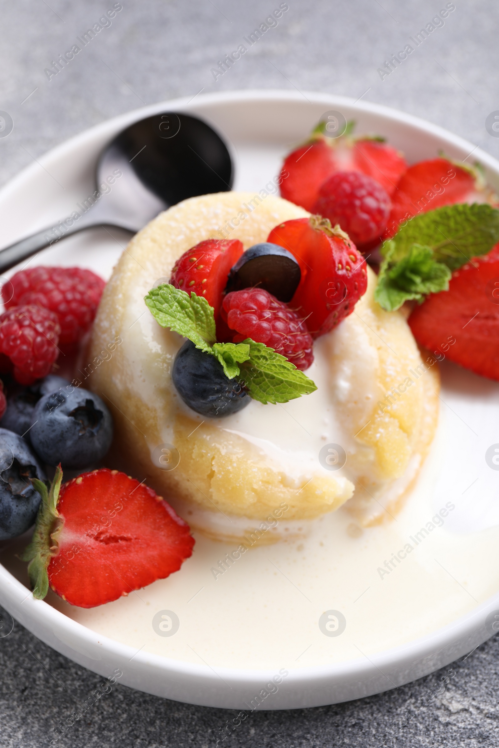 Photo of Delicious vanilla fondant served with fresh berries on grey textured table, closeup