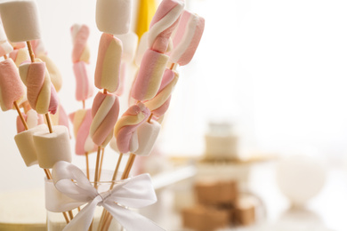 Photo of Tasty marshmallow on wooden sticks with bow in room decorated for birthday party, closeup