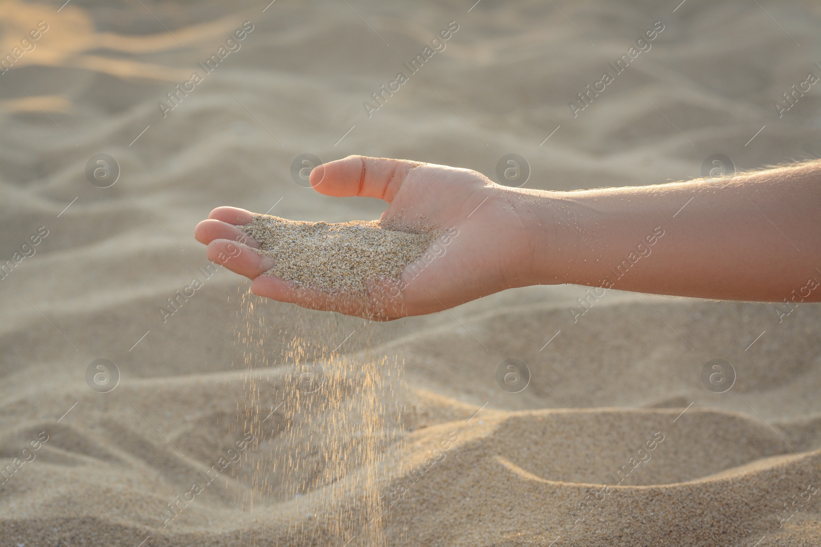 Photo of Girl pouring sand from hand outdoors, closeup. Fleeting time concept