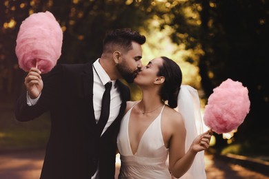 Image of Newlywed couple with cotton candies kissing in park