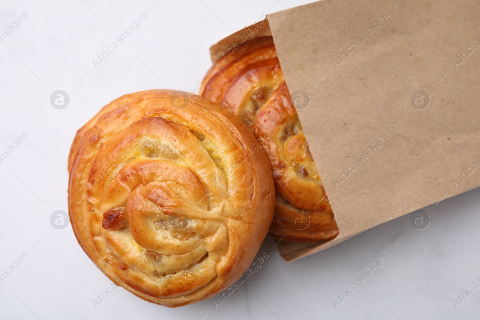 Photo of Paper bag with delicious rolls on white table, top view. Sweet buns