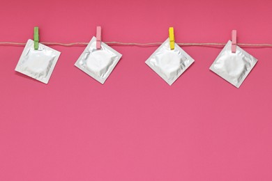 Photo of Clothesline with packaged condoms on pink background, space for text. Safe sex
