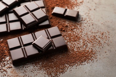 Photo of Delicious dark chocolate and cocoa powder on grey table, closeup