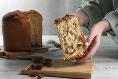 Woman holding slice of delicious Panettone cake with raisins at white wooden table, closeup and space for text. Traditional Italian pastry