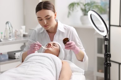 Photo of Cosmetologist applying mask on woman's face in clinic