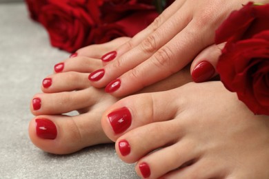 Photo of Woman with stylish red toenails after pedicure procedure and rose flowers on grey textured floor, closeup