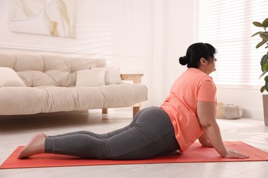 Photo of Overweight mature woman doing exercise on yoga mat at home
