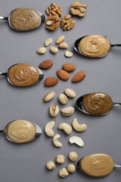 Photo of Tasty nut butters in spoons and raw nuts on gray table, flat lay