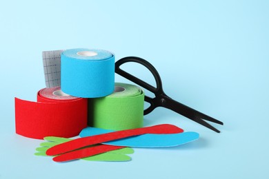 Photo of Scissors, bright kinesio tape rolls and pieces on light blue background