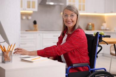 Woman in wheelchair using computer at table in home office