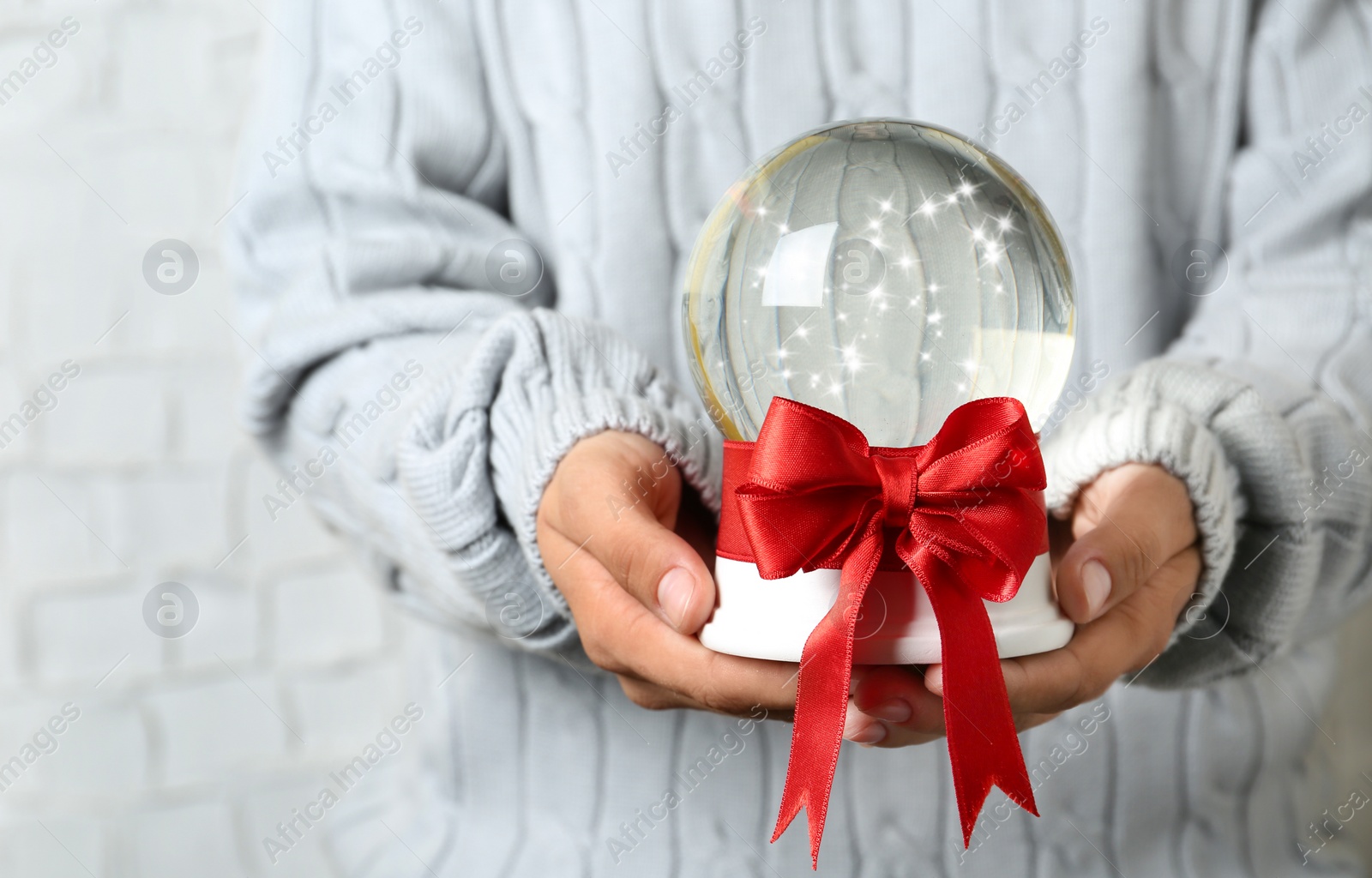 Photo of Woman holding snow globe with red bow on blurred background, closeup