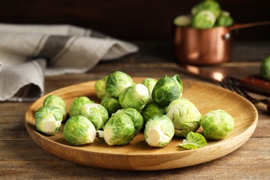 Plate with fresh Brussels sprouts on wooden table, closeup