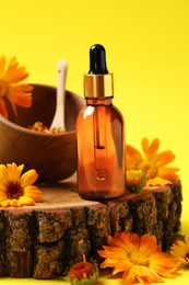Photo of Bottle of essential oil and beautiful calendula flowers on yellow background