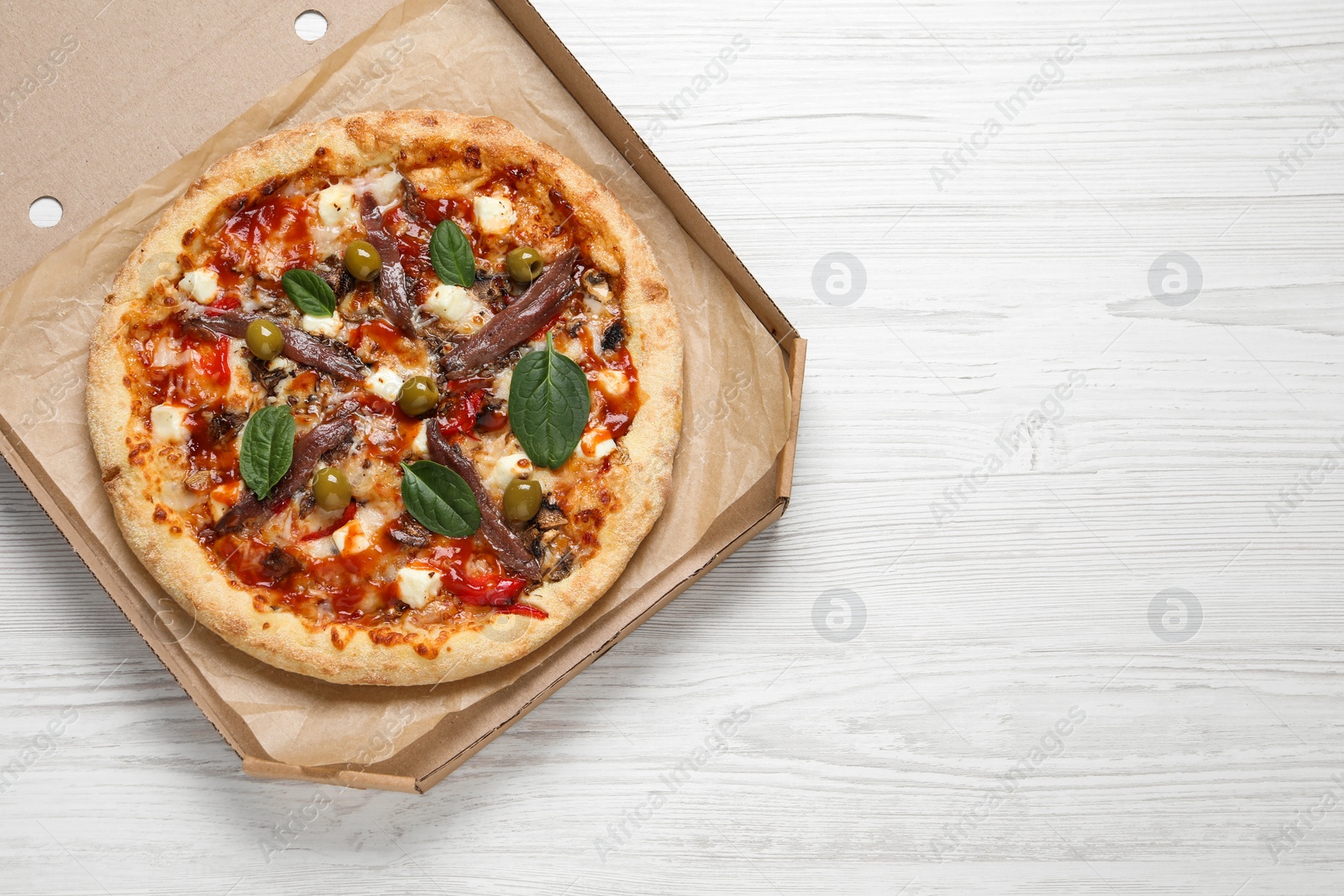 Photo of Tasty pizza with anchovies, basil and olives on white wooden table, top view. Space for text