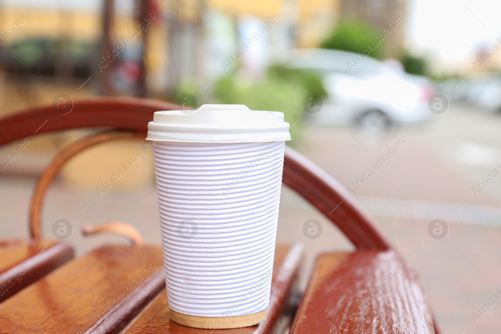 Photo of Paper cup of coffee on wooden bench outdoors. Takeaway drink