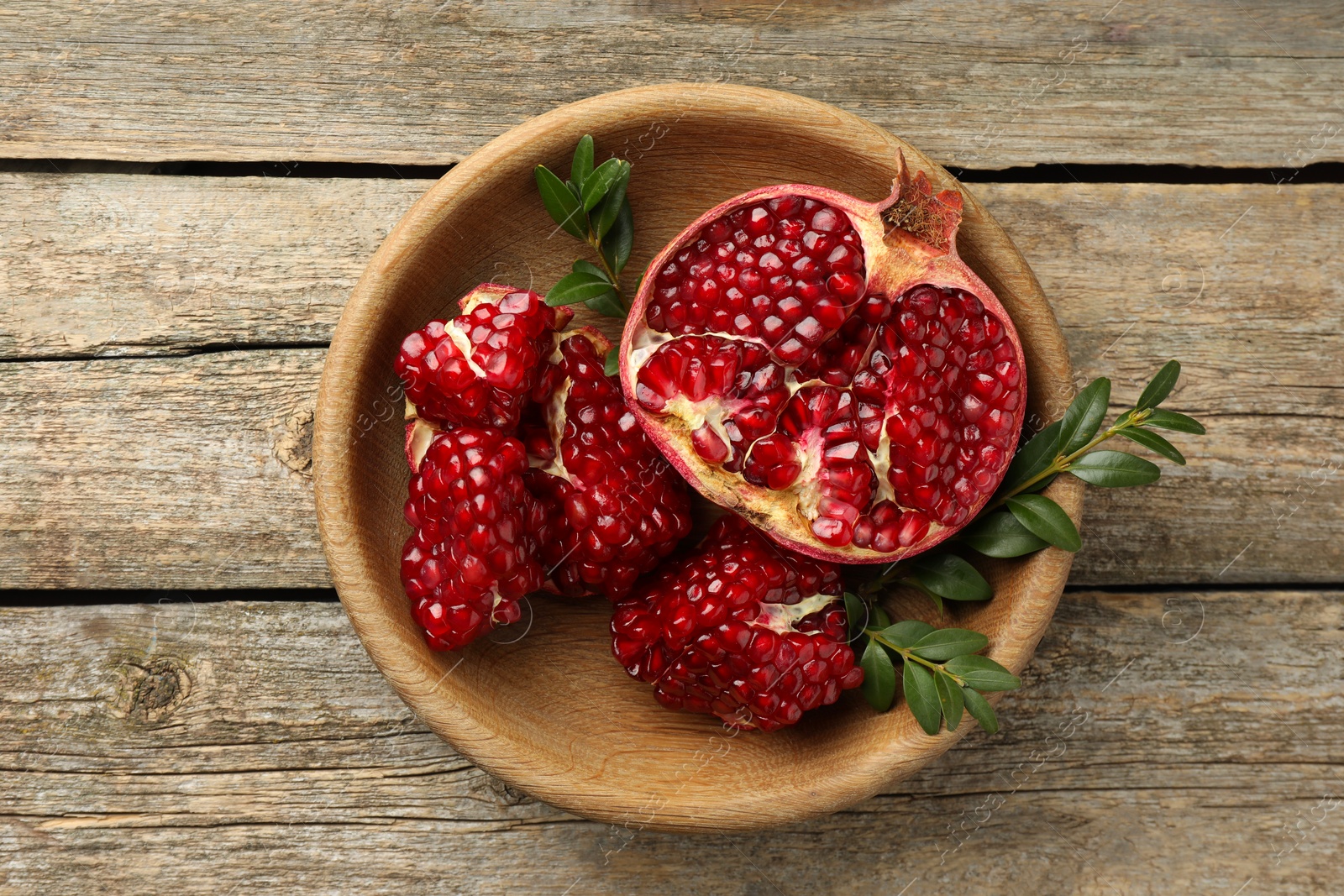 Photo of Cut fresh pomegranate and green leaves on wooden table, top view