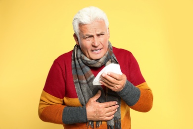 Senior man coughing on yellow background. Cold symptoms