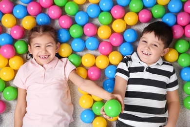 Cute children playing with colorful balls on floor indoors, top view