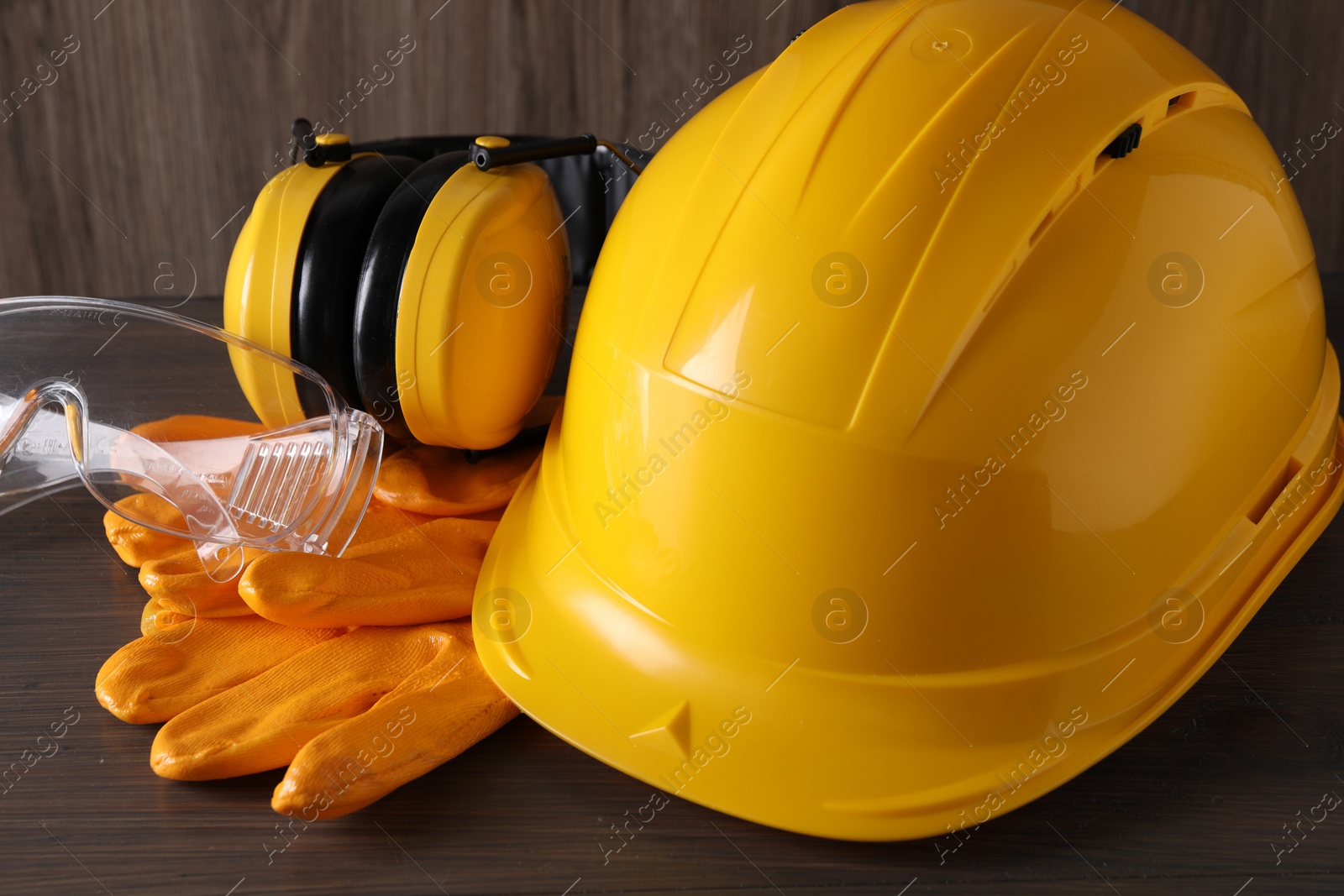 Photo of Hard hat, earmuffs, goggles and gloves on wooden table, closeup. Safety equipment