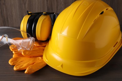 Photo of Hard hat, earmuffs, goggles and gloves on wooden table, closeup. Safety equipment