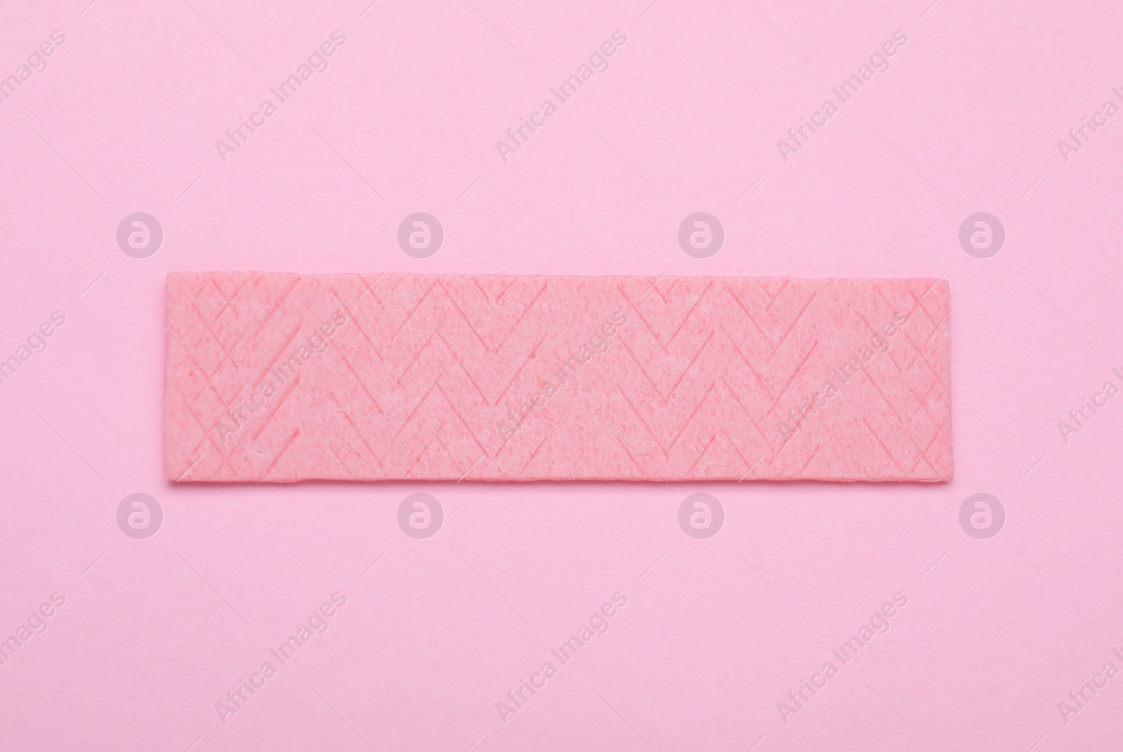 Photo of Stick of tasty chewing gum on pink background, top view