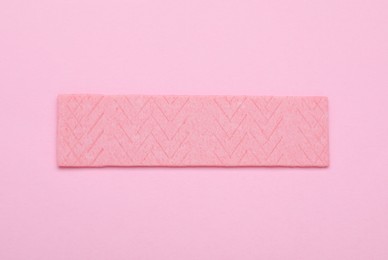 Photo of Stick of tasty chewing gum on pink background, top view