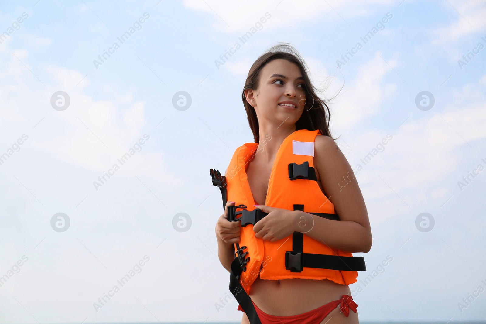 Photo of Beautiful young lifeguard putting on life vest against sky