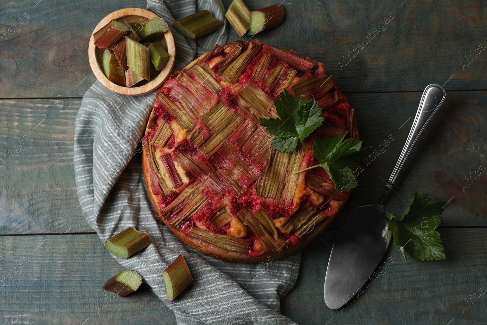 Photo of Freshly baked rhubarb pie, cut stalks and cake server on wooden table, flat lay