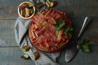 Photo of Freshly baked rhubarb pie, cut stalks and cake server on wooden table, flat lay