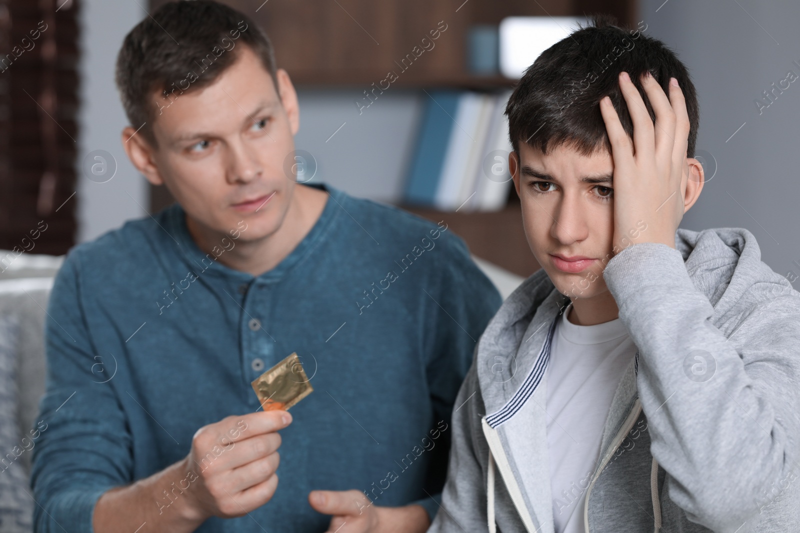 Photo of Father talking with his teenage son about contraception at home. Sex education concept