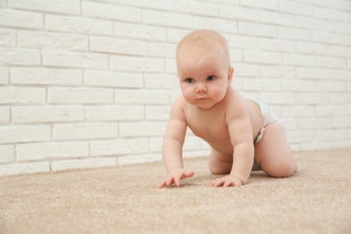 Photo of Cute little baby crawling on carpet near brick wall, space for text