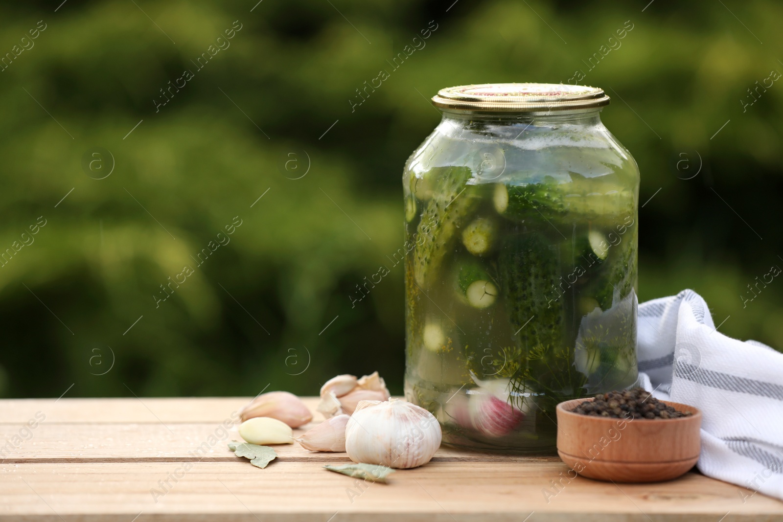 Photo of Jar of delicious pickled cucumbers and ingredients on wooden table against blurred background. Space for text