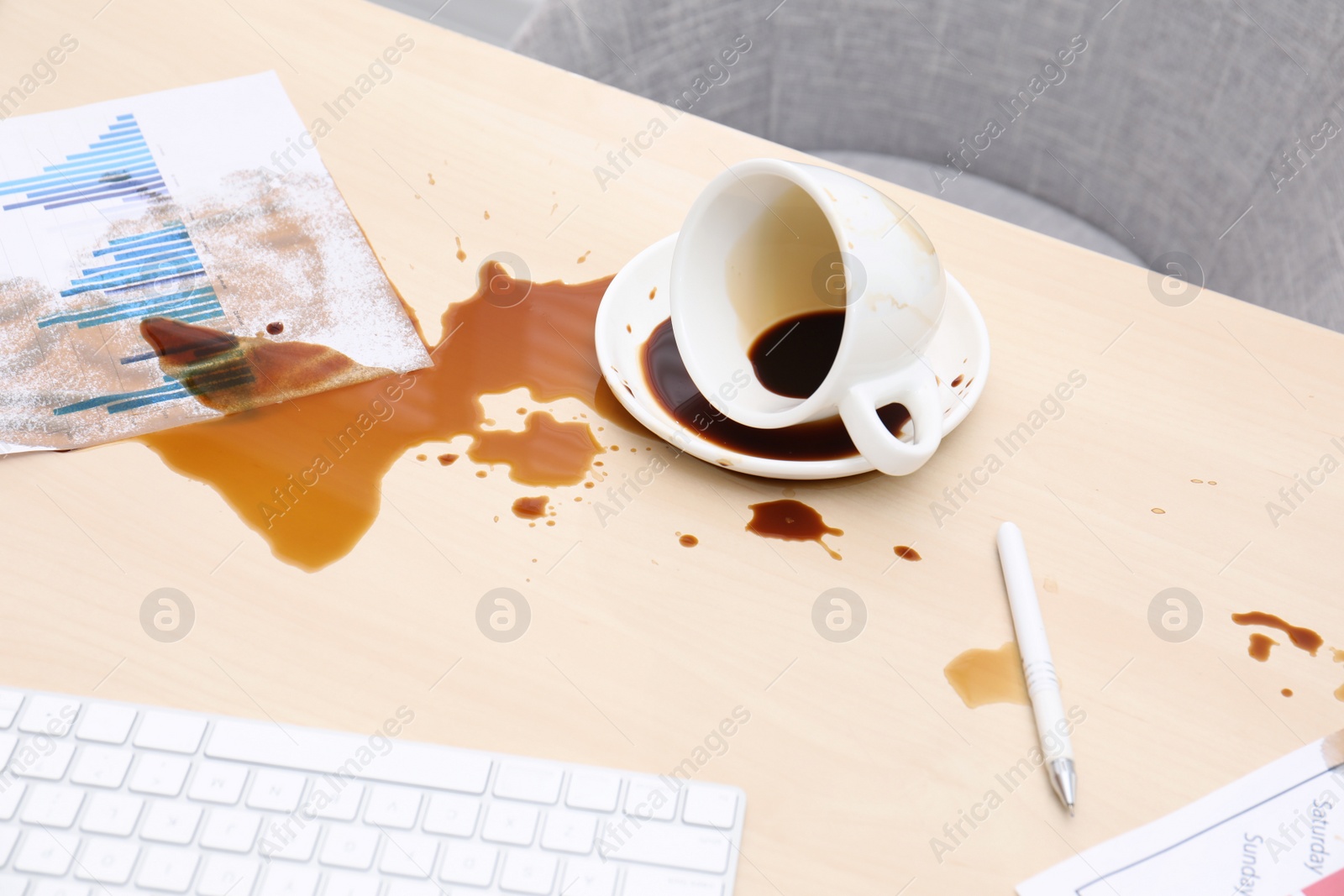 Photo of Cup with saucer and coffee spill on wooden office desk