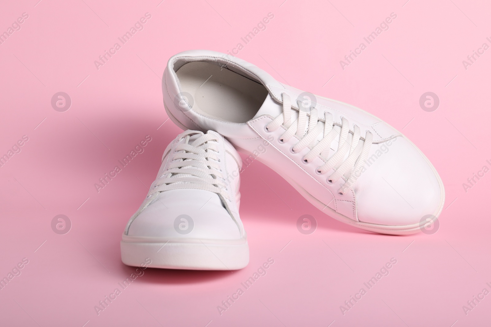 Photo of Pair of stylish white sneakers on pink background