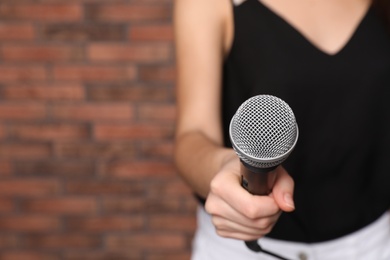 Photo of Young woman holding microphone near brick wall, closeup view with space for text