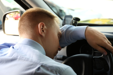 Tired young man sleeping on steering wheel in his car