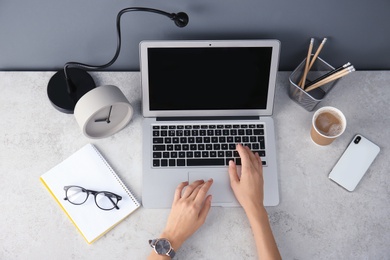 Photo of Female blogger using laptop at table, top view. Blank screen for mockup